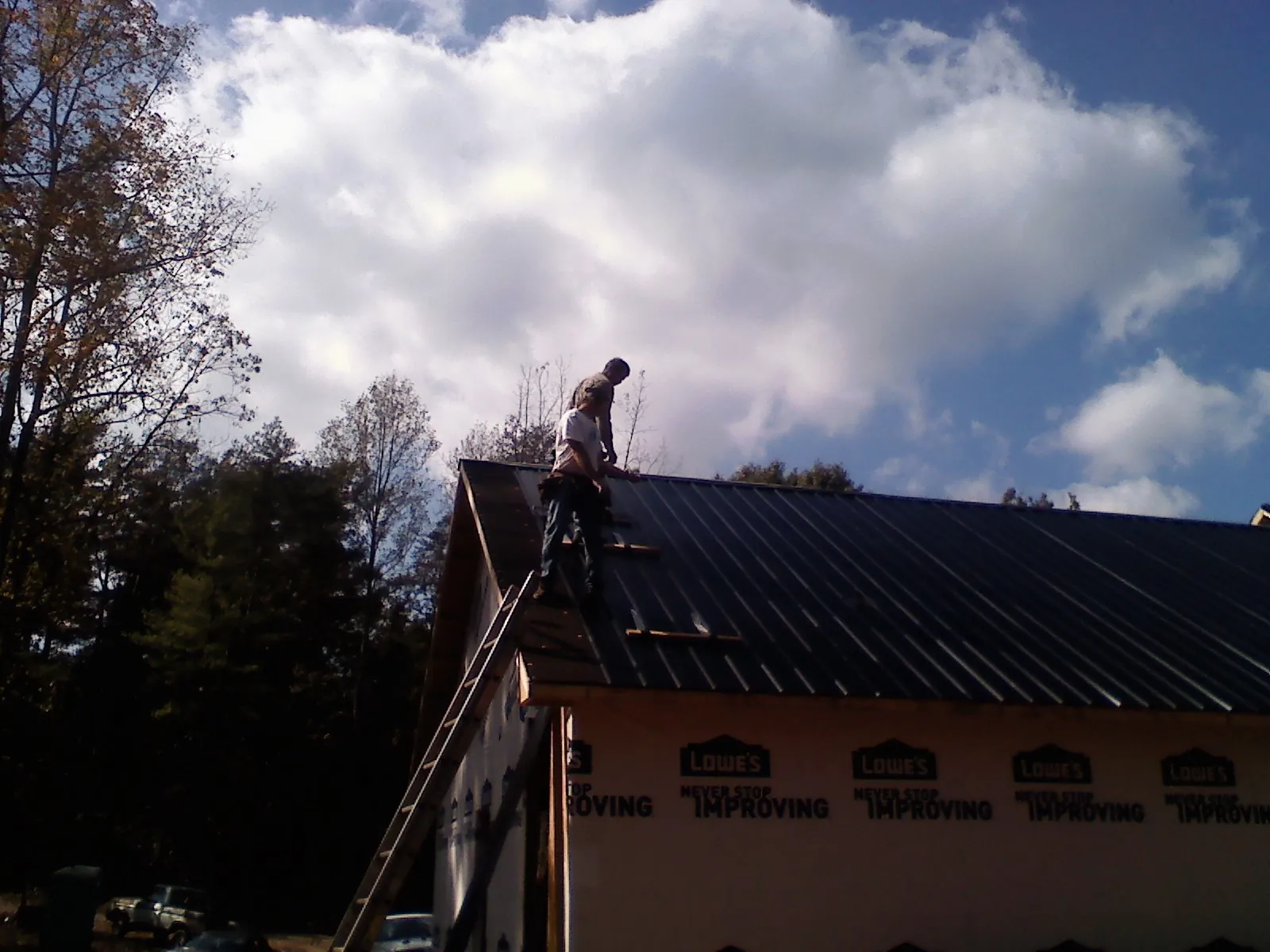 Roofer fastening dark metal panels high against a cloudy sky, from a Roof Inspection job in Melrose